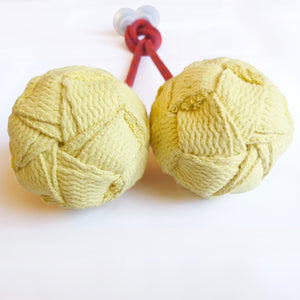 Two yellow fabric balls connected by red cord.