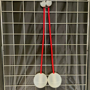 Two white balls connected by red cords, hanging on a grid.
